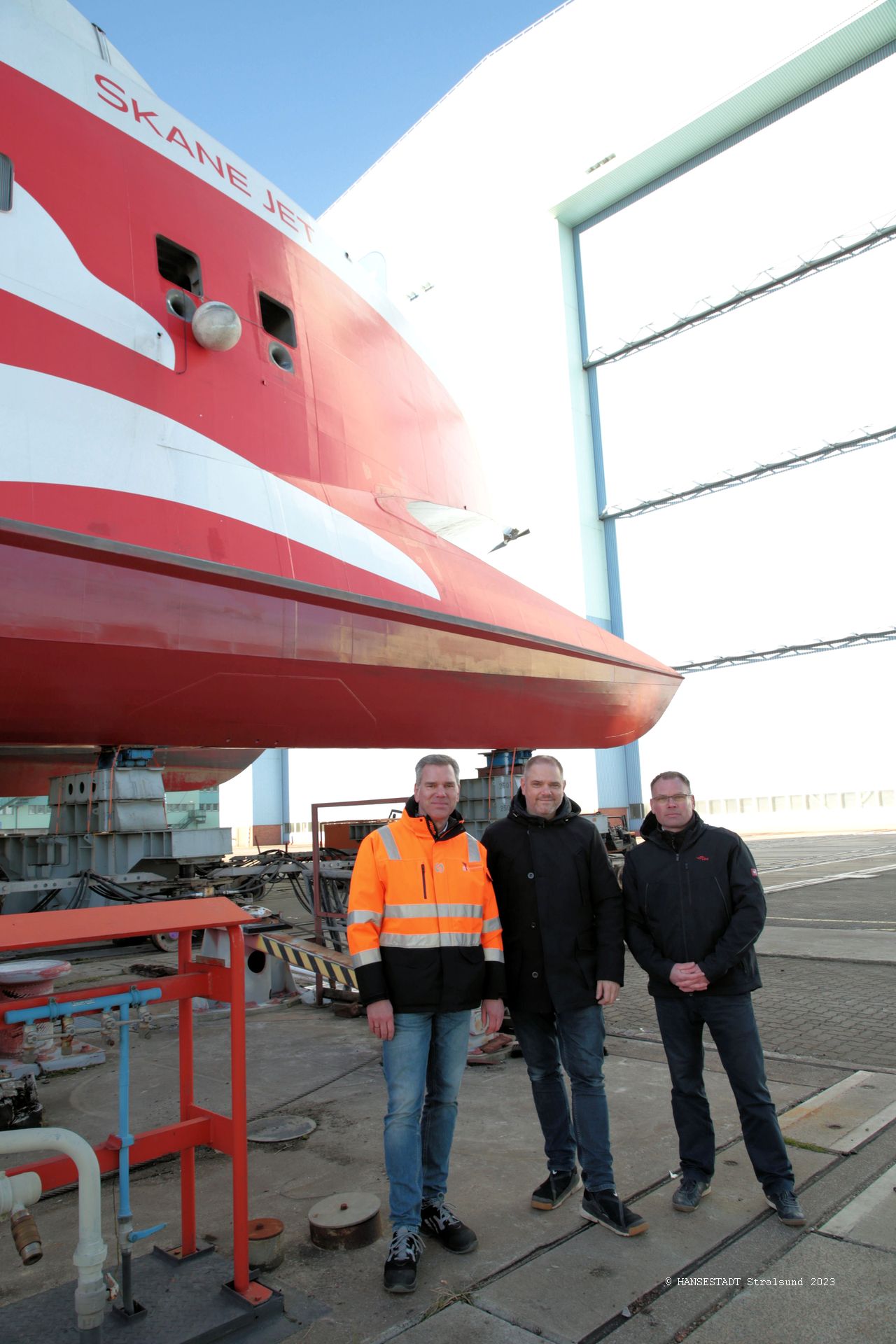 Vor dem Skane Jet und der Werfthalle, in die der Katamaran anschließend rollt v.l.n.r. Carsten Stellamanns, Geschäftsführer Fosen Yard, Oberbürgermeister Alexander Badrow und FRS Baltic GmbH Geschäftsführer Moritz Bruns Vor dem Skane Jet und der Werfthalle, in die der Katamaran anschließend rollt v.l.n.r. Carsten Stellamanns, Geschäftsführer Fosen Yard, Oberbürgermeister Alexander Badrow und FRS Baltic GmbH Geschäftsführer Moritz Bruns